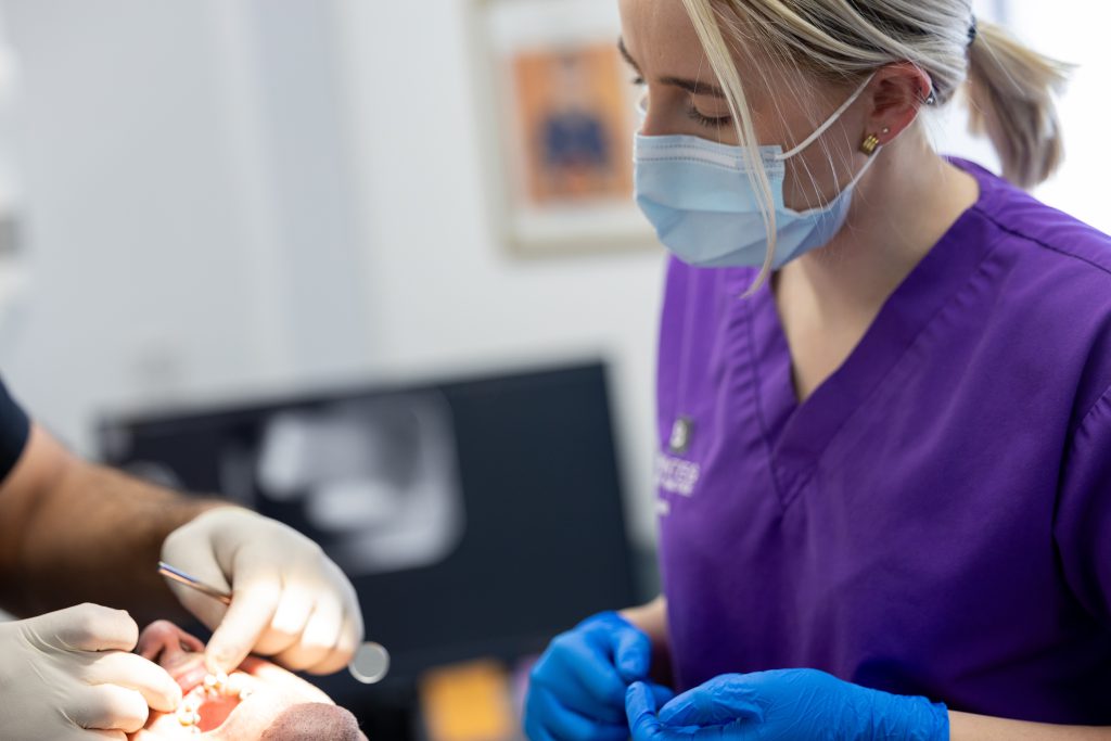 Dental Nurse Work Experience: Image shows dental nurse with mask and gloves assisting dentist with patient.