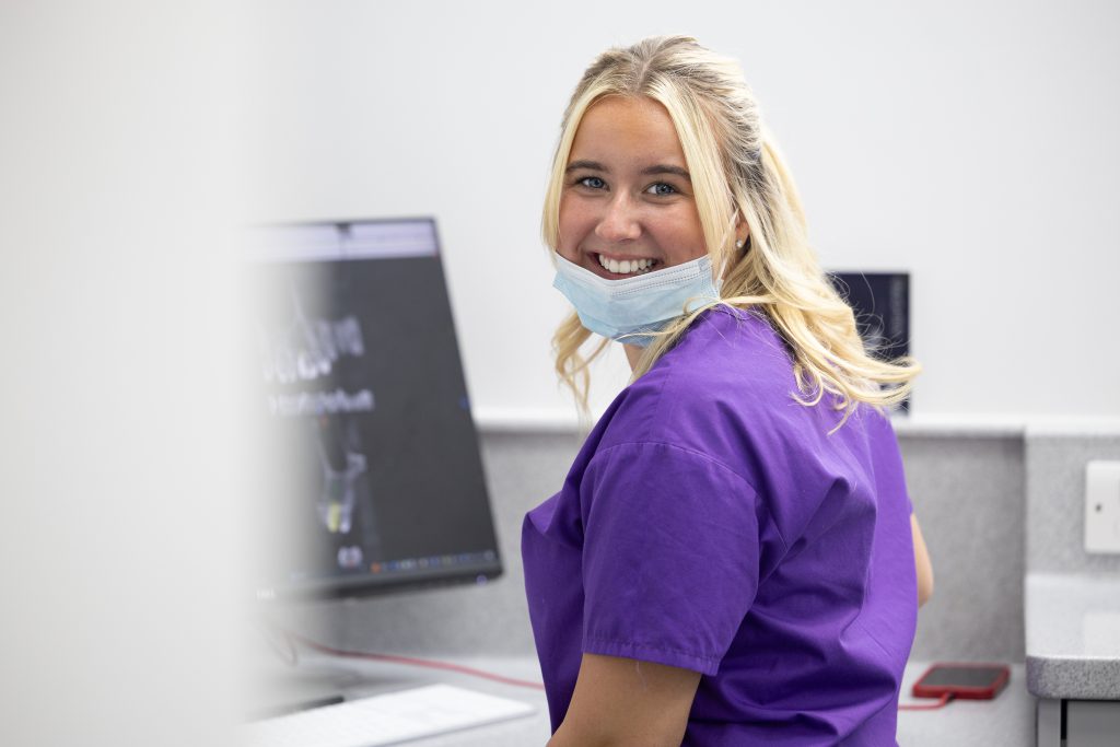 Dental Nurse smiling, sitting at surgery desk and reviewing x-rays.