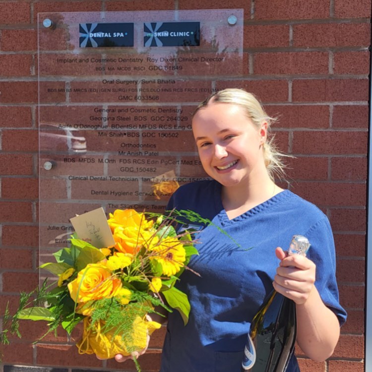 Dental Nurse Molly, smiling and celebrating passing her nurse qualification, holding a bouquet of flowers and champagne.