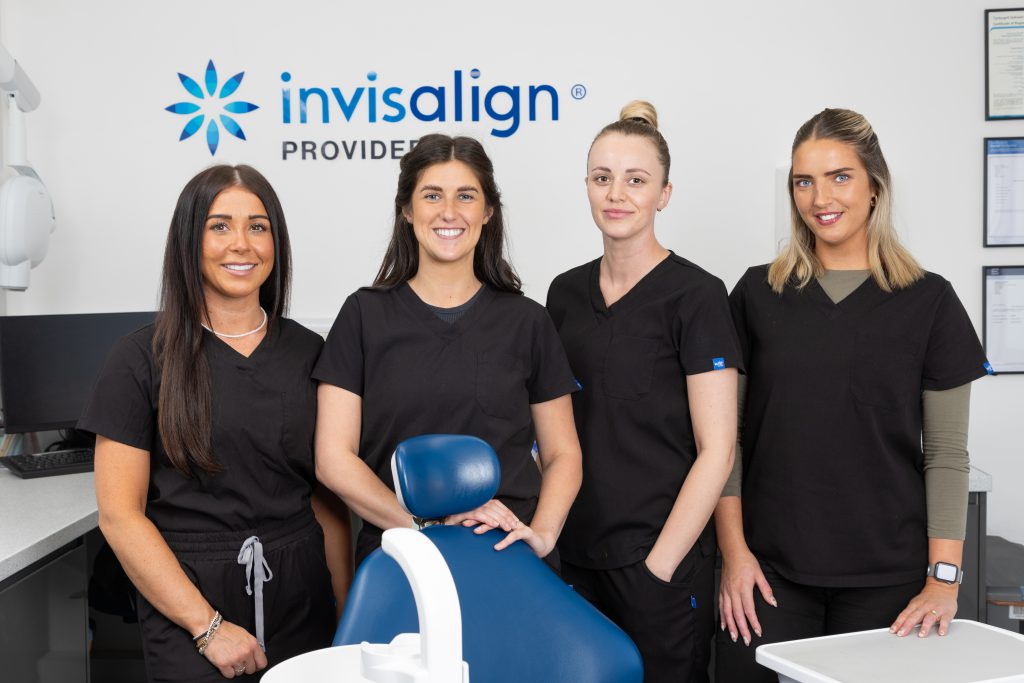 4 dental nurses stood around a dental chair smiling brightly at camera