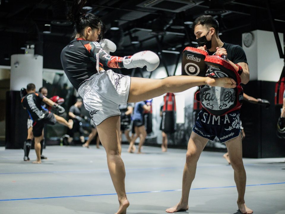 Image of a woman kicking pads with her trainer in a mixed martial arts gym.
